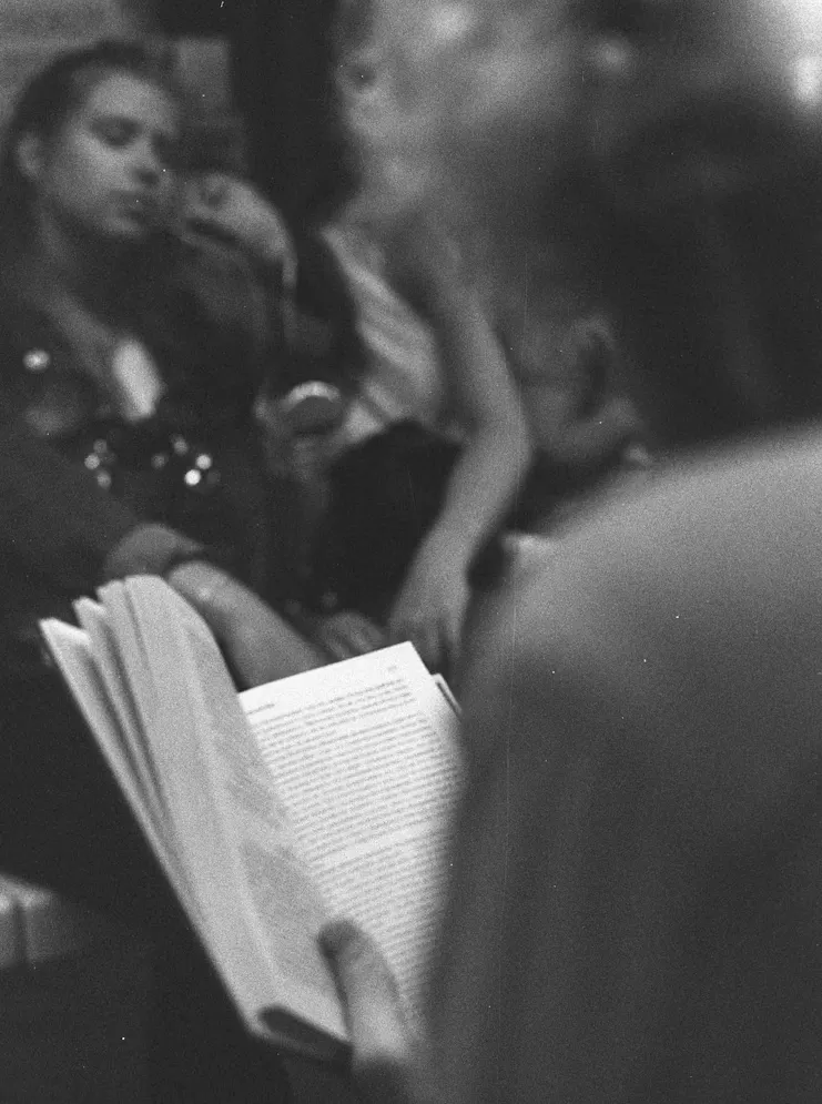 A traveler reading a book, half-turned toward a conversation nearby.